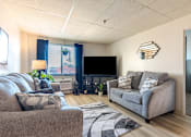 Thumbnail 2 of 13 - A living room with a grey couch and a television.
