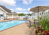 Thumbnail 18 of 26 - A pool surrounded by a white fence and a patio with chairs and an umbrella.