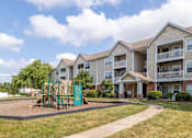 Thumbnail 22 of 26 - A playground with a green slide is in front of apartment buildings.