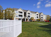 Thumbnail 23 of 26 - A white picket fence in front of a large apartment building.