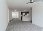 Thumbnail 2 of 17 - A spacious living room with a ceiling fan and a kitchen area in the background.