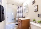 Thumbnail 5 of 13 - A bathroom with a white tub, a wooden vanity, and striped shower curtain.