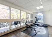 Thumbnail 9 of 13 - A gym room with a treadmill, exercise bike, and a chair.