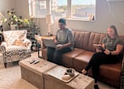 Thumbnail 5 of 35 - Two people sitting on a couch in a living room with a coffee table in front of them.