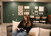 Thumbnail 1 of 67 - a woman sitting on a couch reading a book in a living room  at Timber Ridge, Forest Lake, MN