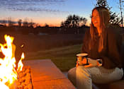 Thumbnail 51 of 67 - a woman sitting next to a fire with a cup of coffee  at Timber Ridge, Forest Lake, 55025