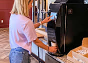 Thumbnail 52 of 67 - a woman putting a cup into an automatic coffee machine  at Timber Ridge, Forest Lake
