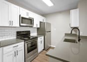 Thumbnail 8 of 20 - Modern galley kitchen with sleek white cabinets, stainless steel appliances, subway tile backsplash, and quartz countertops.