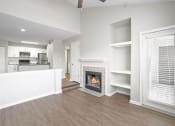 Thumbnail 9 of 20 - Open-concept living space with vaulted ceilings, a cozy fireplace, built-in shelving, and modern hardwood-style flooring adjacent to the kitchen.