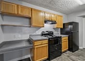 Thumbnail 4 of 40 - Kitchen with black appliances, wood cabinetry, spacious countertops, and built-in shelving in a 3-bedroom, 2-bath apartment at Gregory Cove in Jacksonville, FL.