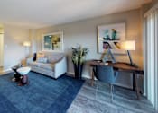 Thumbnail 6 of 82 - A modern living room with a white sofa, a grey armchair, a wooden desk, and a blue rug.
