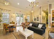 Thumbnail 10 of 17 - A living room with a black couch, a dining table with chairs, and a coffee table with a vase of flowers.