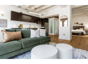 Thumbnail 5 of 18 - a living room with a green couch and two white stools