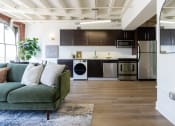 Thumbnail 3 of 18 - a living room with a couch and a kitchen with stainless steel appliances