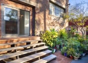 Thumbnail 56 of 57 - the front of a brick house with a large wooden porch and potted plants