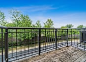 Thumbnail 33 of 42 - A wooden deck with a metal railing overlooks a road and greenery.