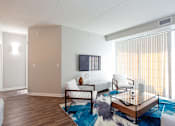 Thumbnail 28 of 42 - A living room with a white couch, a wooden coffee table, and a flat screen TV mounted on the wall.