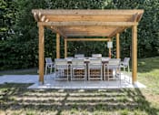 Thumbnail 23 of 32 - A wooden pergola with a large table and chairs by two BBQ grills at The Crossings at Russett in Laurel, MD