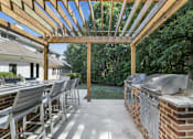 Thumbnail 24 of 32 - A wooden pergola with a large table and chairs by two BBQ grills at The Crossings at Russett in Laurel, MD