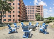 Thumbnail 17 of 30 - an outdoor patio with blue chairs and a fire pit in front of an apartment building