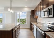 Thumbnail 4 of 44 - A kitchen with brown cabinets and a view of the outdoors through a sliding glass door at Sonder Point 50+ Apartments, Minnesota, 55430