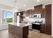 Thumbnail 5 of 44 - A kitchen with brown cabinets and a granite countertop at Sonder Point 50+ Apartments, Minnesota