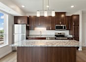 Thumbnail 27 of 44 - A kitchen with brown cabinets and a granite countertop at Sonder Point 50+ Apartments, Brooklyn Center, Minnesota