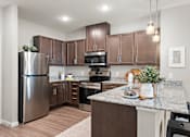 Thumbnail 1 of 40 - A kitchen with brown cabinets and a stainless steel refrigerator.at Decatur Landing I & II, Brooklyn Park, MN 55445