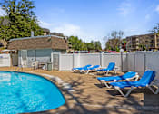 Thumbnail 20 of 32 - a swimming pool with blue chaise lounge chairs and a poolside building with apartments at Heritage Hills Apartments, Bloomington Minnesota