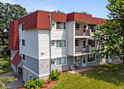 Thumbnail 27 of 32 - a white and red apartment building with a yard and trees at Heritage Hills Apartments, Minnesota
