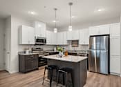 Thumbnail 3 of 19 - an open kitchen with a large island and stainless steel refrigerator at The Landing at Amber Fields Apartments, Rosemount, Minnesota