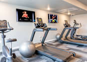 Thumbnail 17 of 51 - four treadmills and exercise balls in a gym with televisions on the wall at Technology Park Apartments, Rochester, MN