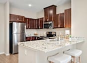 Thumbnail 2 of 44 - A kitchen with a granite countertop and white stools at The Winslow 62+ Apartments, West St Paul