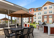Thumbnail 27 of 44 - a patio with an umbrella and a table with chairs and a grill at The Winslow 62+ Apartments, Minnesota