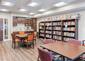 Thumbnail 37 of 44 - a library with tables and chairs and a kitchen and library shelves at The Winslow 62+ Apartments, West St Paul, Minnesota