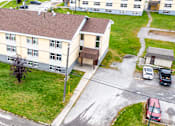 Thumbnail 50 of 57 - A large building with a brown roof is surrounded by a grassy area and a parking lot.