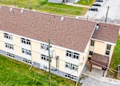 Thumbnail 49 of 57 - A building with a brown roof and a parking lot in front.