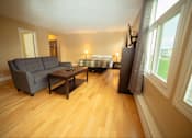 Thumbnail 14 of 57 - A living room with a grey couch and a bed in the background.