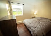 Thumbnail 22 of 57 - A bedroom with a bed, wooden dresser, and a window with a view of the outside.