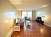 Thumbnail 35 of 57 - A living room with a grey couch, a white end table, a wooden coffee table, and a black television.