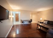 Thumbnail 41 of 57 - A living room with a grey couch, a black chair, a black table, a white tablecloth, a white lamp, a white door, and a white wall.