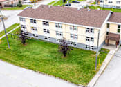 Thumbnail 7 of 28 - A large building with a brown roof is surrounded by a grassy area and a parking lot.