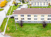Thumbnail 8 of 28 - A large building with a brown roof is surrounded by a grassy area and a few trees.
