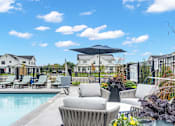 Thumbnail 50 of 113 - A pool surrounded by chairs and umbrellas with houses in the background.