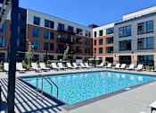 Thumbnail 19 of 61 - A pool surrounded by sun loungers in front of apartment buildings.