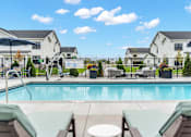 Thumbnail 56 of 113 - A pool with lounge chairs and umbrellas in front of a white building.