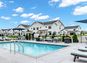 Thumbnail 49 of 113 - A swimming pool surrounded by lounge chairs and a fence with houses in the background.
