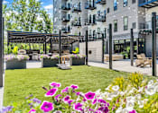 Thumbnail 7 of 71 - A patio area with a table and chairs is surrounded by a grassy area with purple flowers.