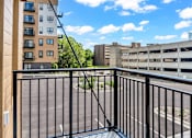 Thumbnail 68 of 71 - A balcony with a black railing overlooks a parking garage and buildings.