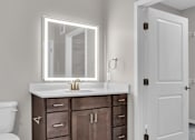 Thumbnail 66 of 71 - A bathroom with a white toilet, a sink with a mirror above it, and a white door.